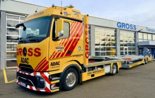 Gelber ADAC-Mobilitäts-Lkw mit auffälligen Streifen vor einem modernen Gebäude der Firma GROSS in Dresden.