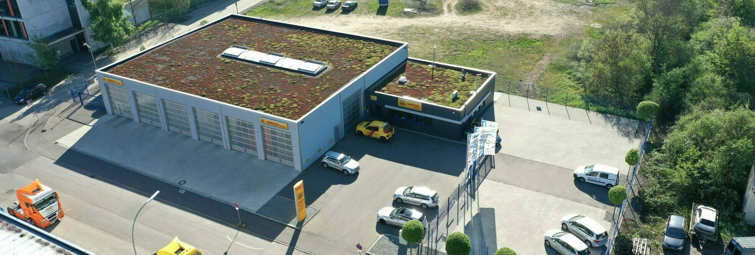 Gebäudekomplex mit bepflanztem Dach, umgeben von geparkten Autos, in einer städtischen, grünen Umgebung.
