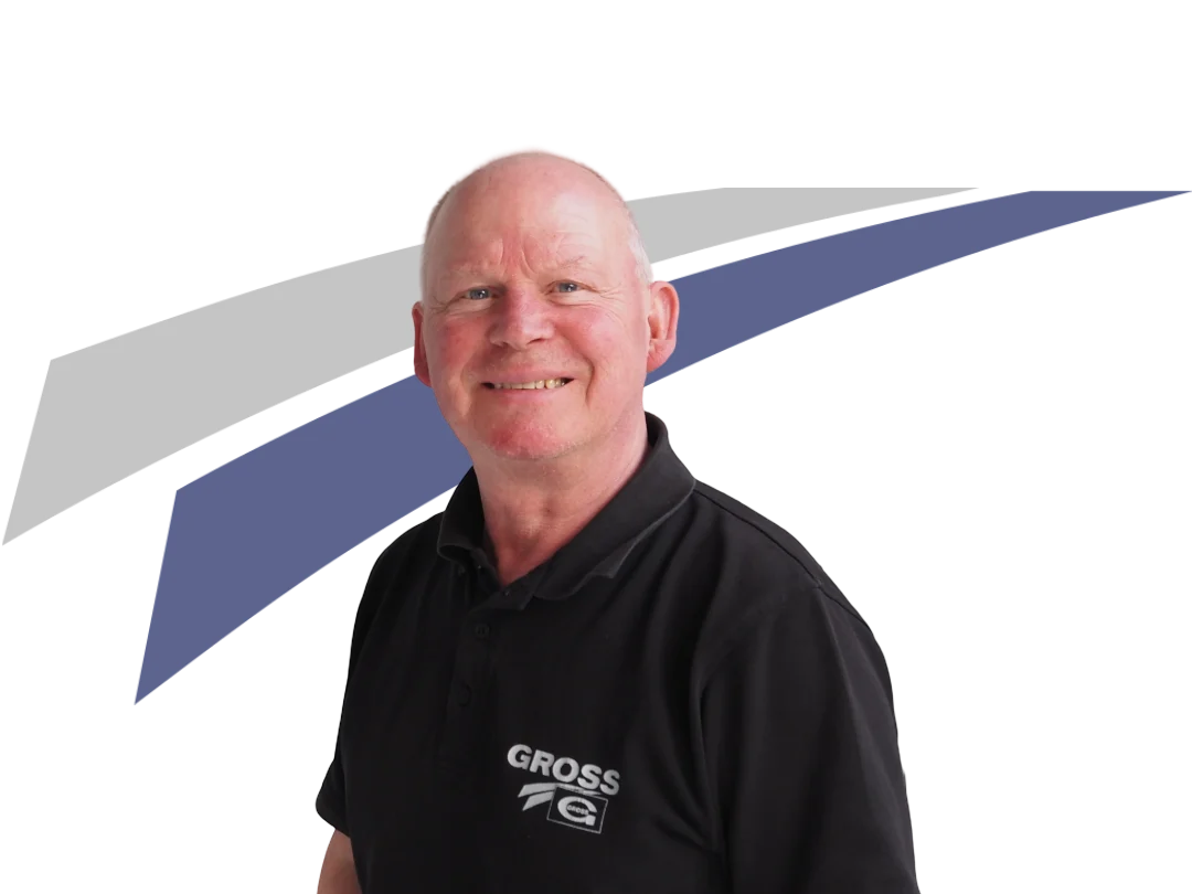 Mann mit Glatze und freundlichem Lächeln trägt ein schwarzes Polohemd mit dem Aufdruck GROSS, vor neutralem Hintergrund.