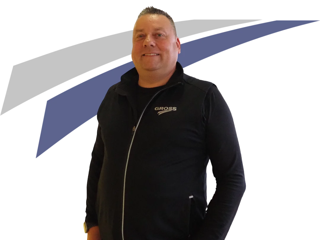 Lächelnder Mann in schwarzer Weste mit Logo, vor einem grafischen Hintergrund in Blau und Grau.