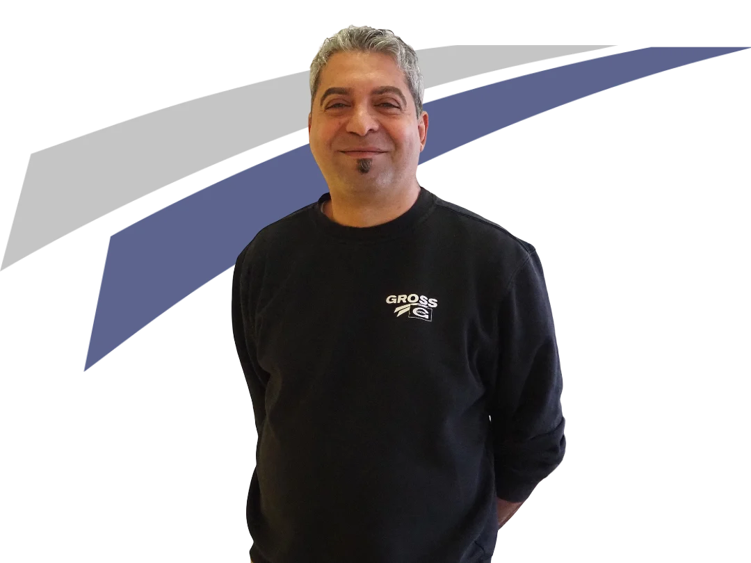 Ein lächelnder Mann in schwarzem Sweatshirt mit Aufdruck „GROSS“ vor einem grafischen Hintergrund in Blau und Grau.