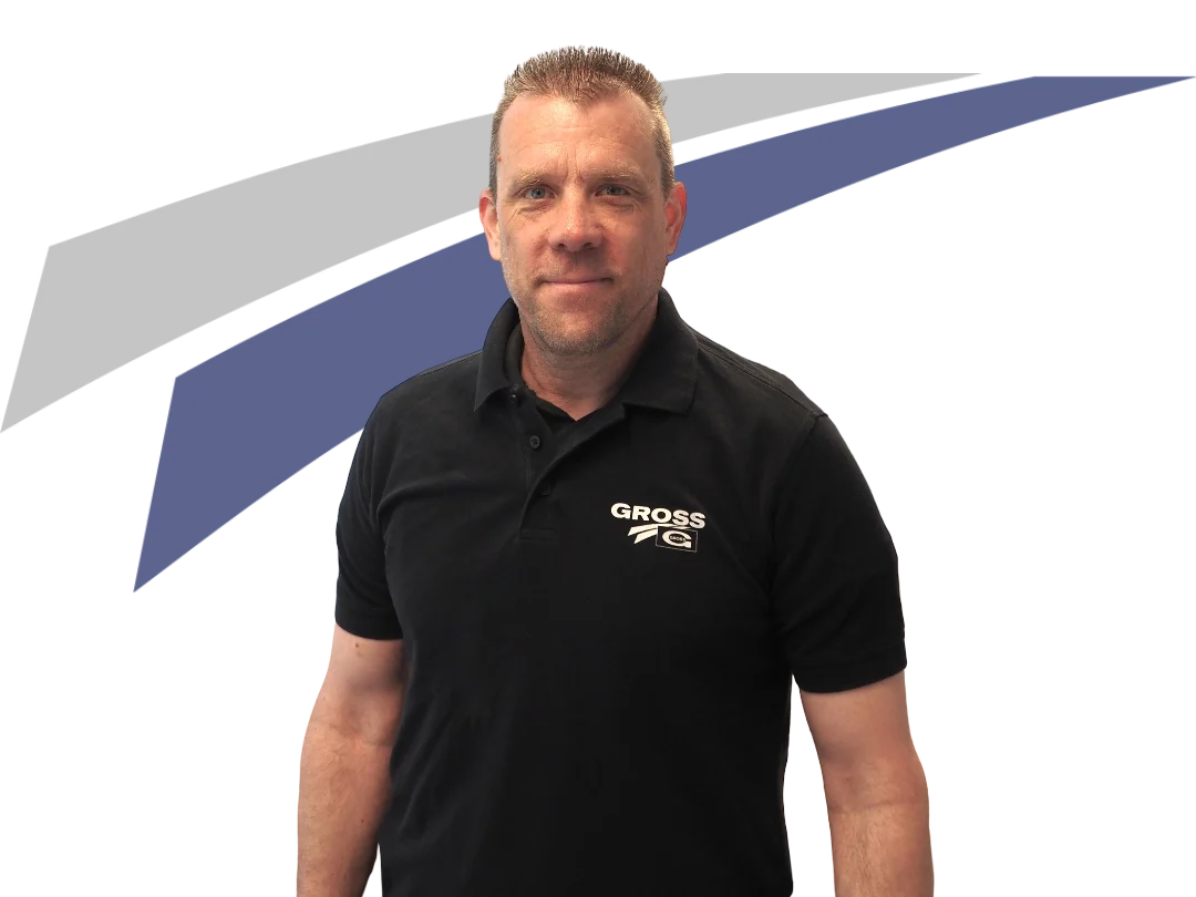 Mann mit kurzem Haar trägt ein schwarzes Polo-Shirt mit dem Aufdruck GROSS, vor einem grafischen, farbigen Hintergrund.