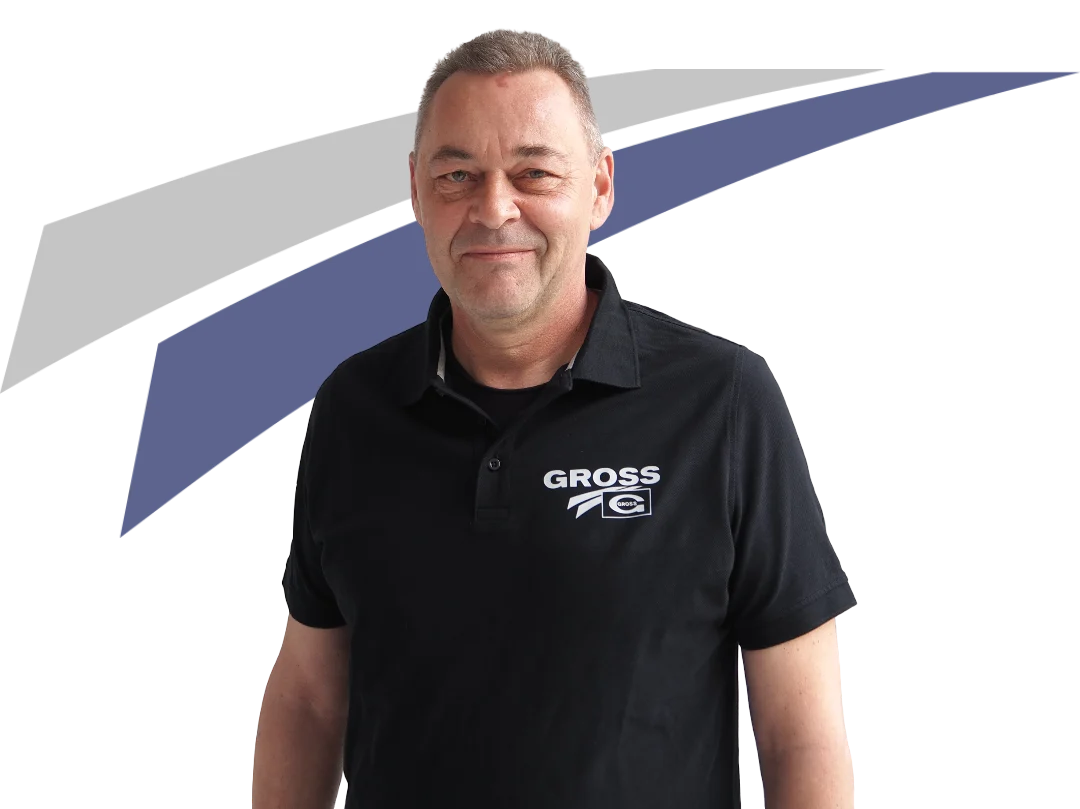 Mann mit kurzem Haar lächelt freundlich in schwarzem Poloshirt mit „GROSS“-Logo und einem farbigen Hintergrund.