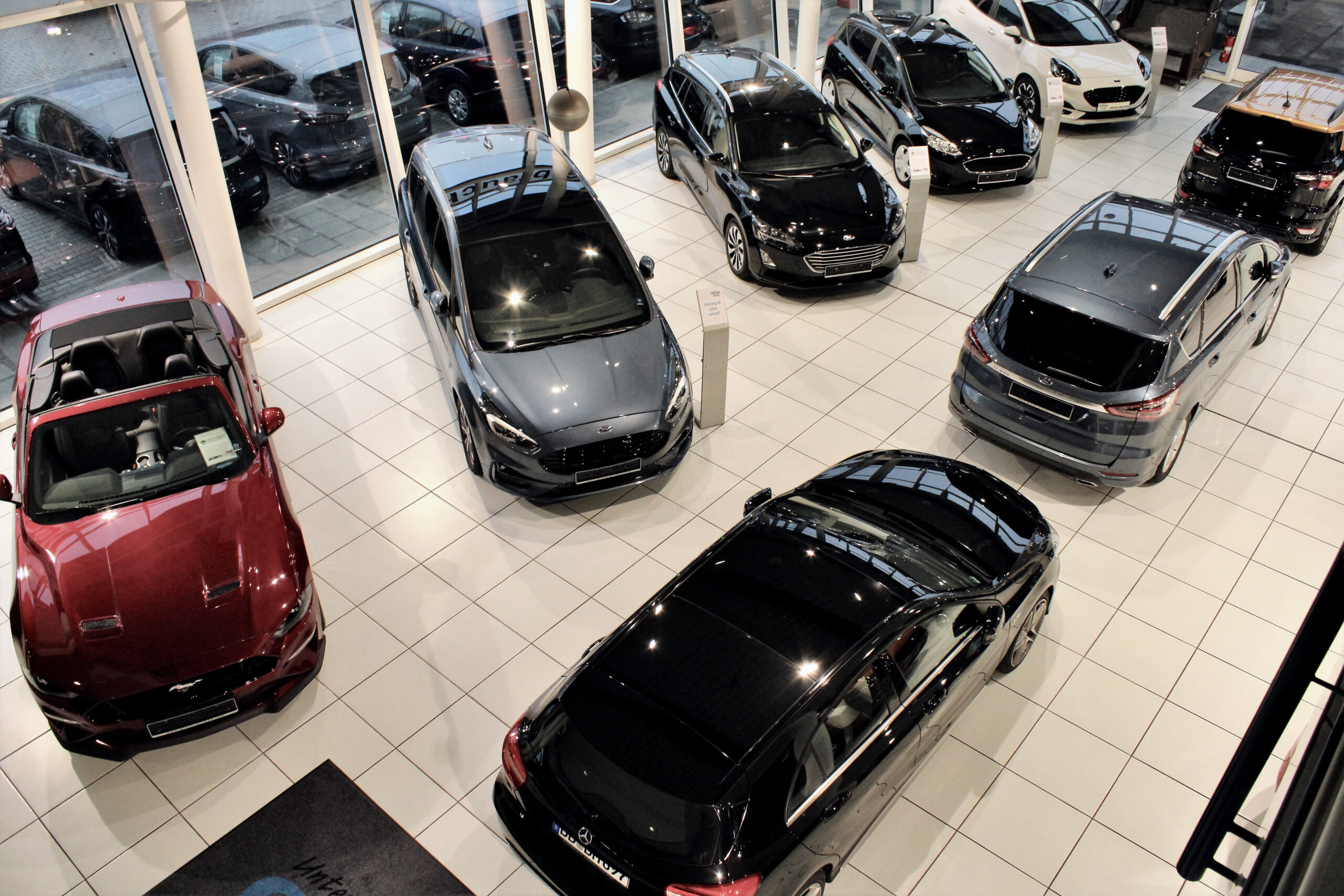 Autohändler mit neun Autos, variierend in Farbe und Modell, auf gefliestem Boden einer hellen Ausstellungshalle.