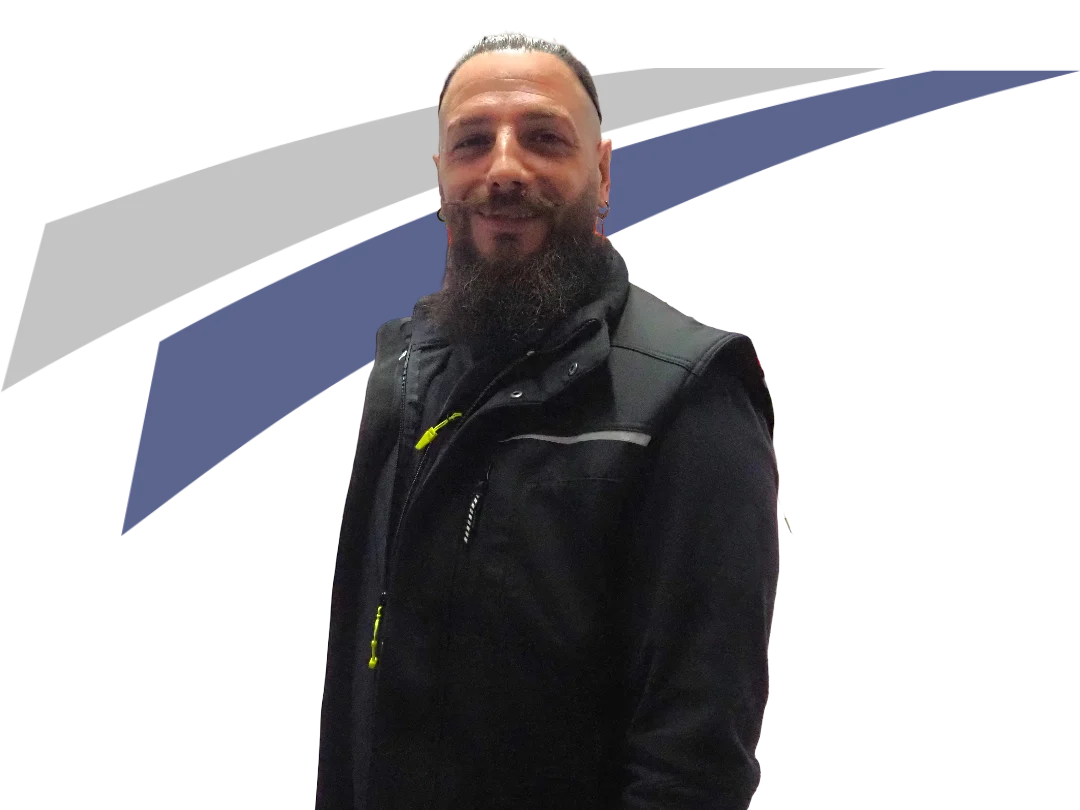 Lächelnder Mann mit Vollbart in schwarzer Jacke, vor einem grauen und blauen Hintergrund.