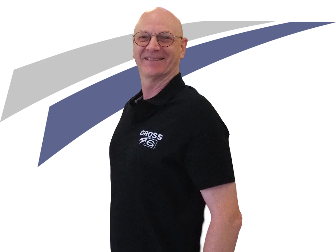 Mann mit Brille in schwarzem Polohemd steht vor grauem und blauen Hintergrund, lächelt freundlich.