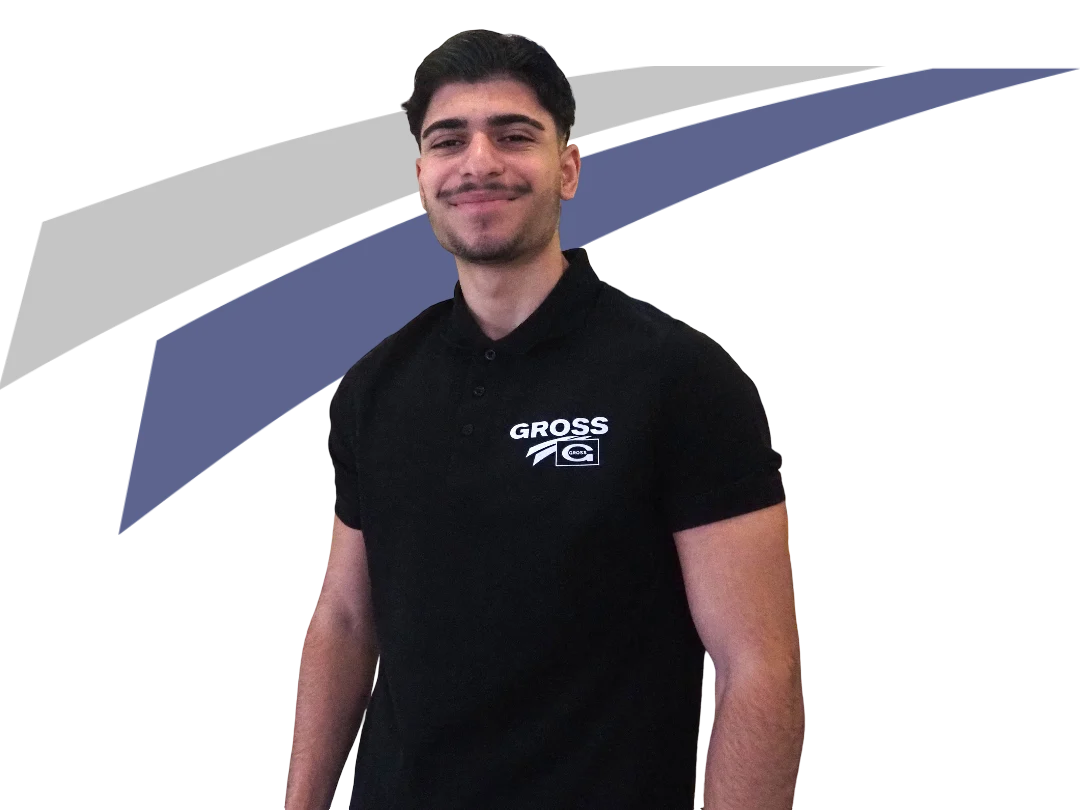 Junger Mann in schwarzem Polohemd mit „GROSS“-Logo, lächelt vor abstraktem Hintergrund in grau und blau.