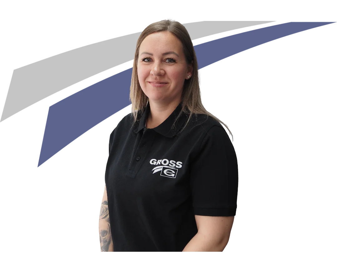 Frau mit Schulterlangem Haar in schwarzem Poloshirt lächelt vor einem neutralen Hintergrund in blauen und grauen Farben.