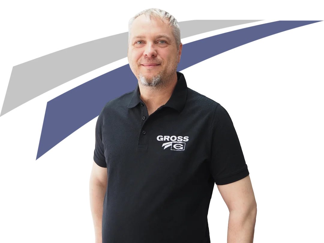 Mann in schwarzem Polo mit Aufdruck GROSS steht vor abstraktem Hintergrund in Grau und Blau.