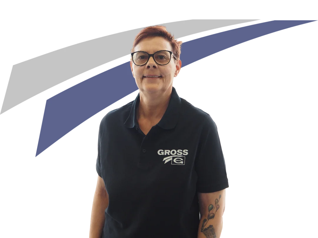 Frau mit Brille in schwarzem Poloshirt steht vor einem grafischen Hintergrund in Blau und Grau. Sie lächelt freundlich.