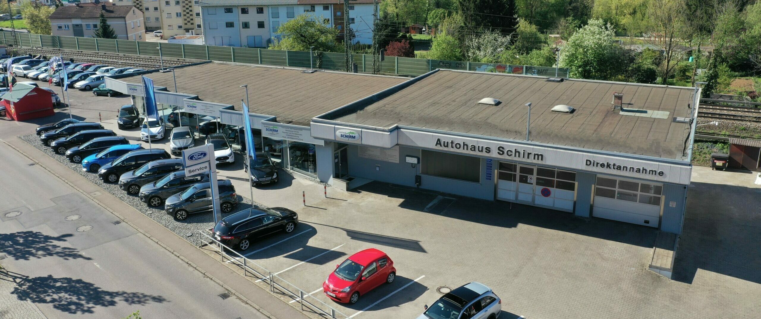 Luftaufnahme eines Autohandels mit vielen geparkten Autos und einem Gebäude mit der Aufschrift „Autohaus Schirm“.