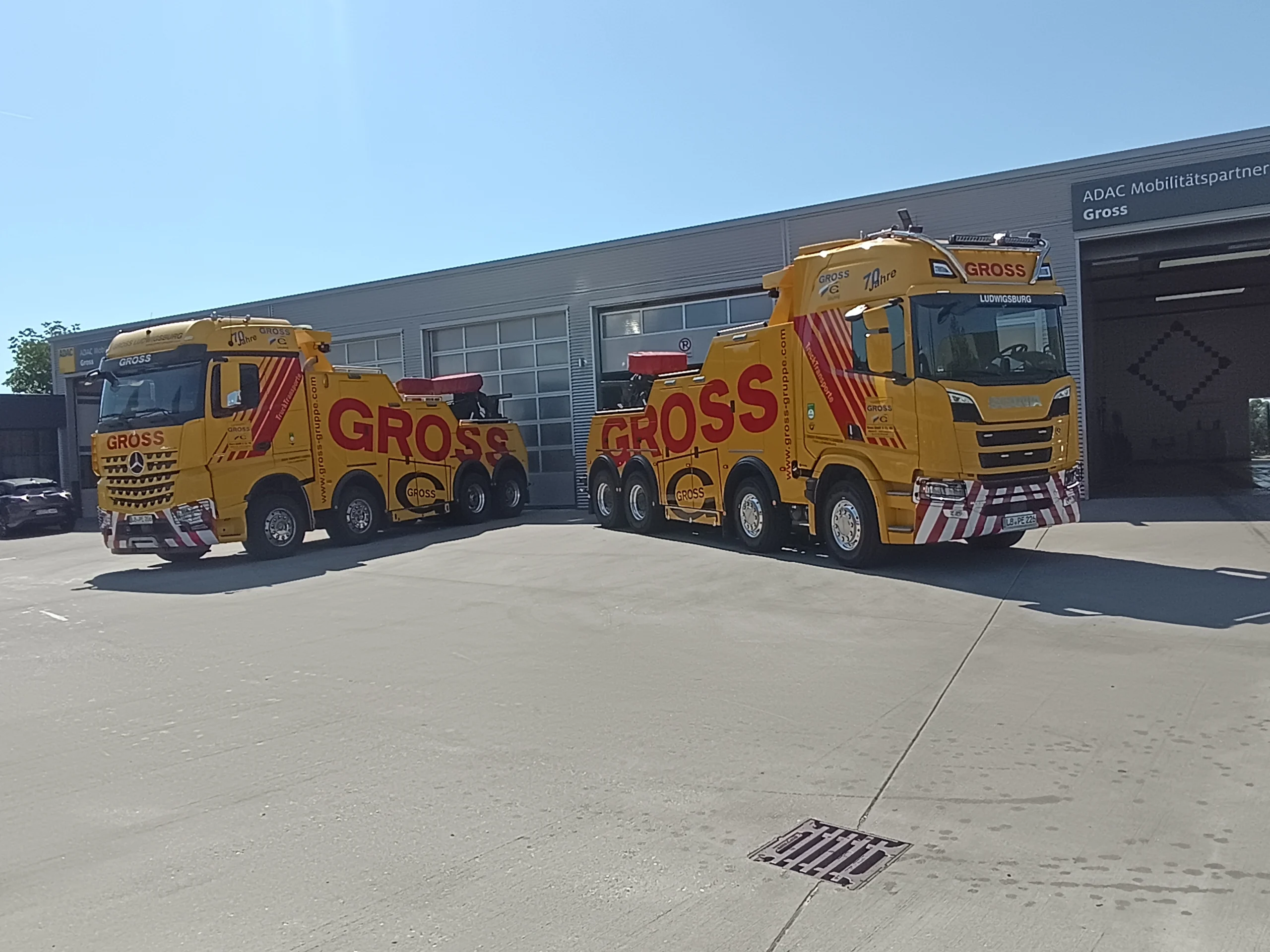 Zwei gelbe Abschleppwagen mit der Aufschrift GROSS vor einer Werkstatt, bei sonnigem Wetter geparkt.