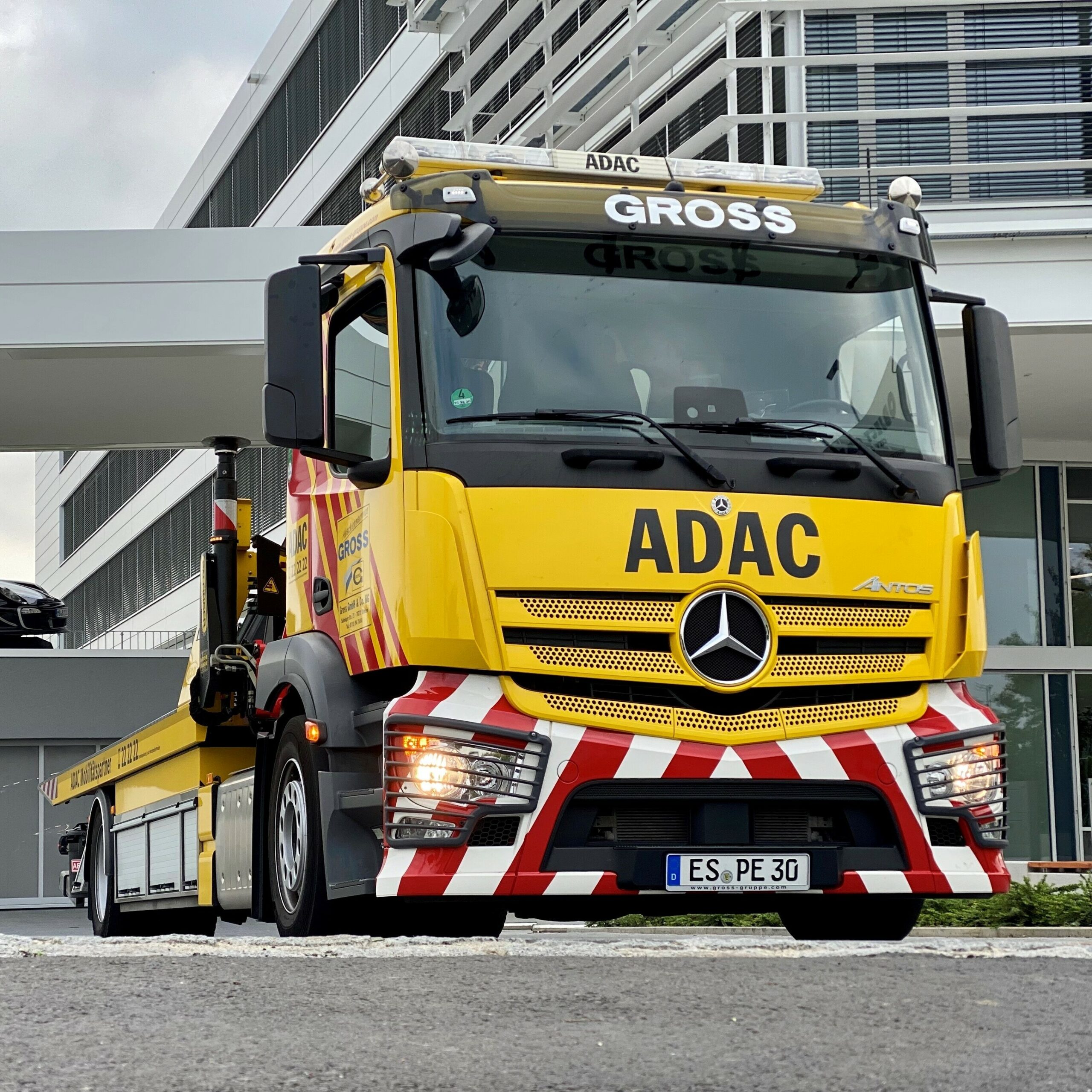 Gelber ADAC-Abschleppwagen mit Mercedes-Logo parkt vor modernem Gebäude, Fahrerhausbeschriftung Gross.