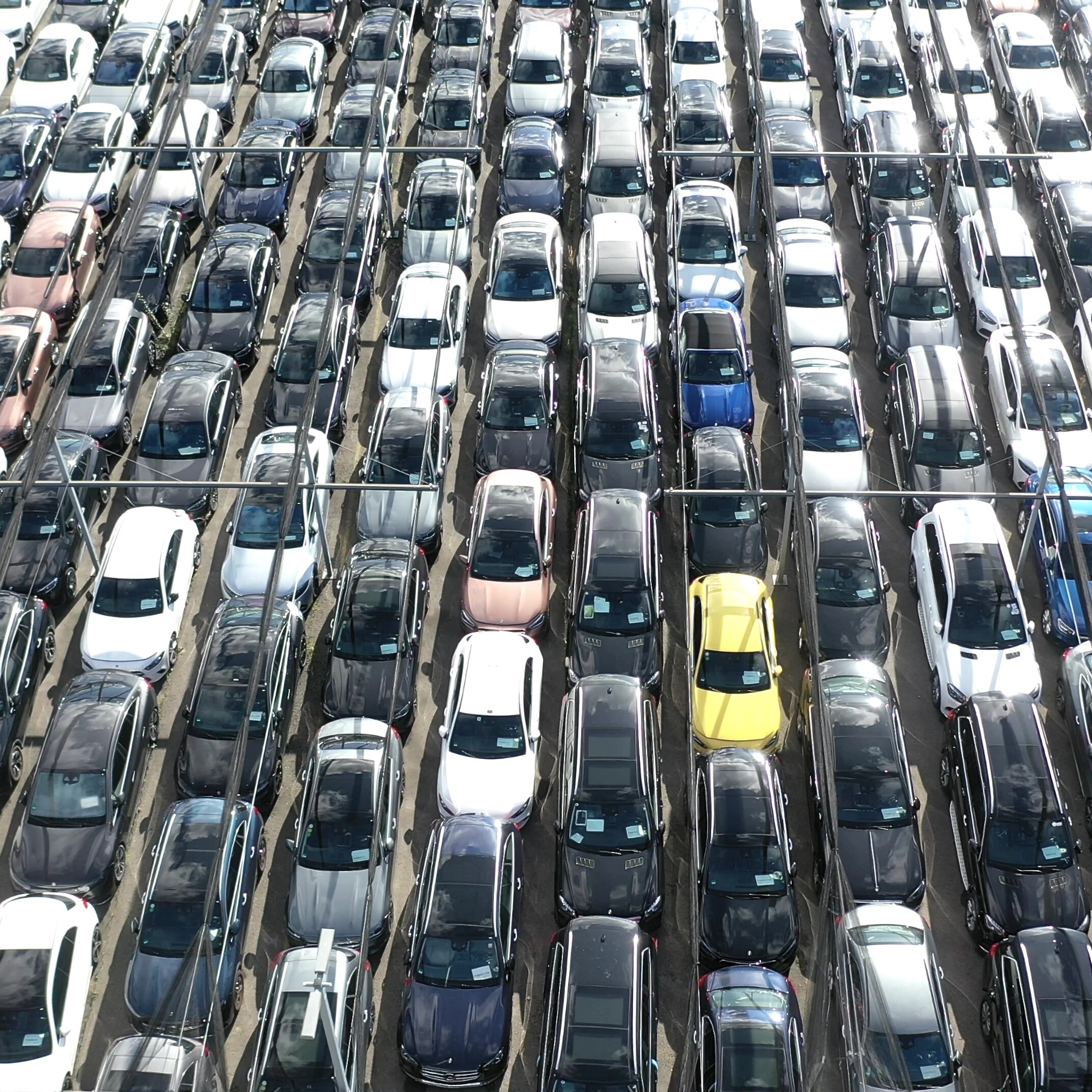 Ein vollgeparkter Parkplatz mit Autos in geordneten Reihen, ein gelbes Auto sticht zwischen dunklen Fahrzeugen hervor.