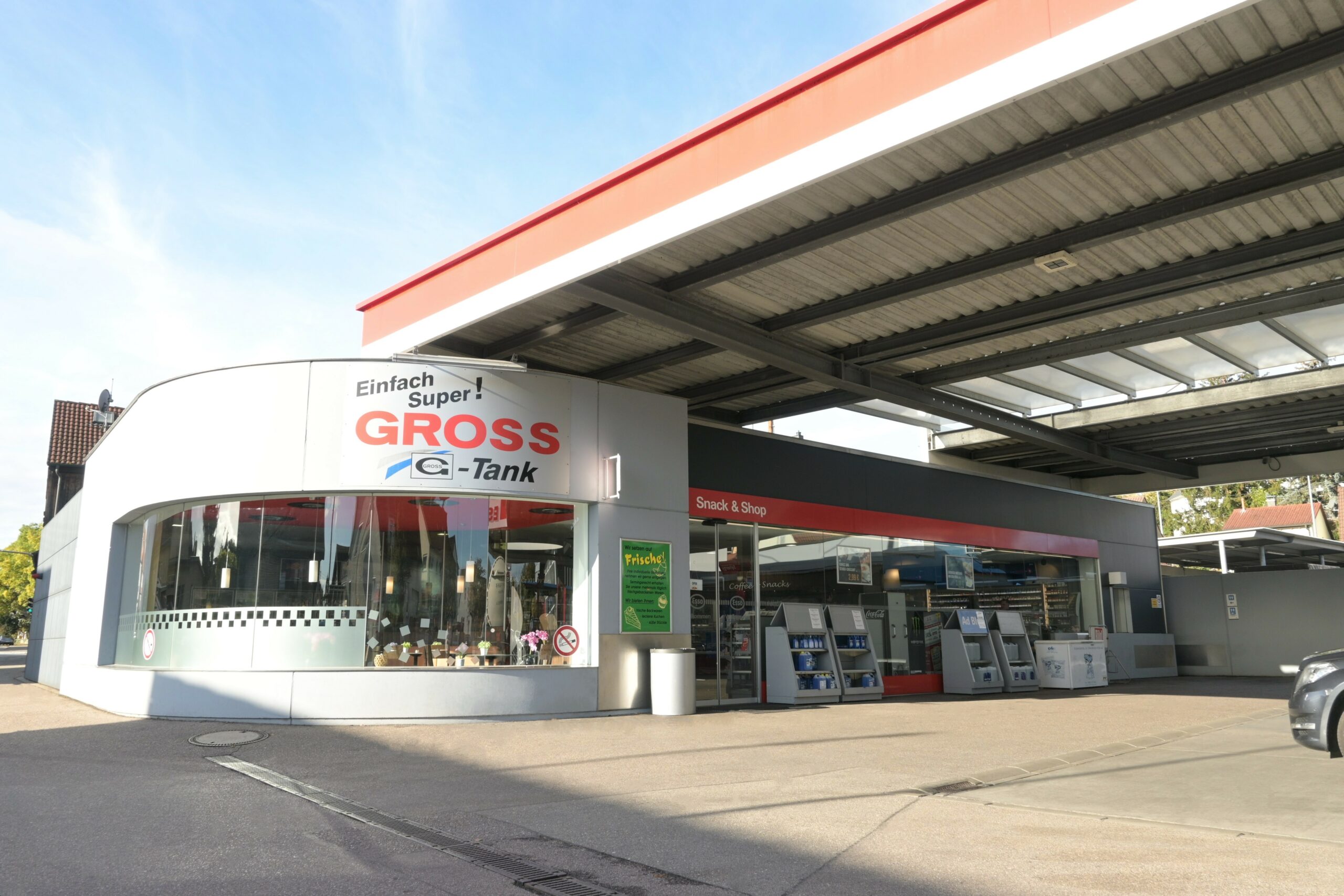 Tankstelle mit Ladenbereich, Glasfront und Überdachung. Schild: Einfach Super! GROSS Tank. Sonniger Tag.