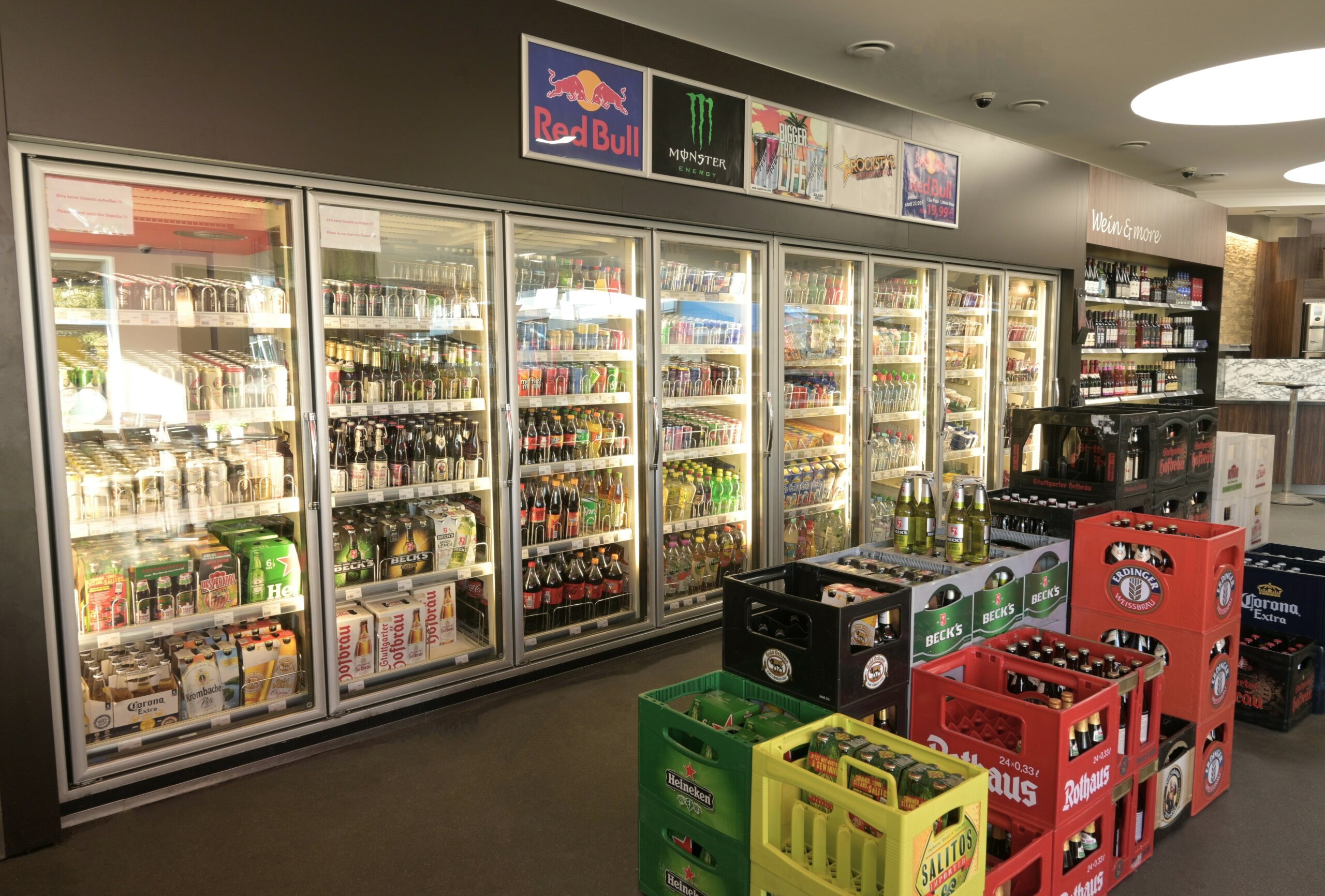Kühlschrank mit verschiedenen Getränken und Getränkekisten, darunter Bier und Softdrinks, in einem Laden.