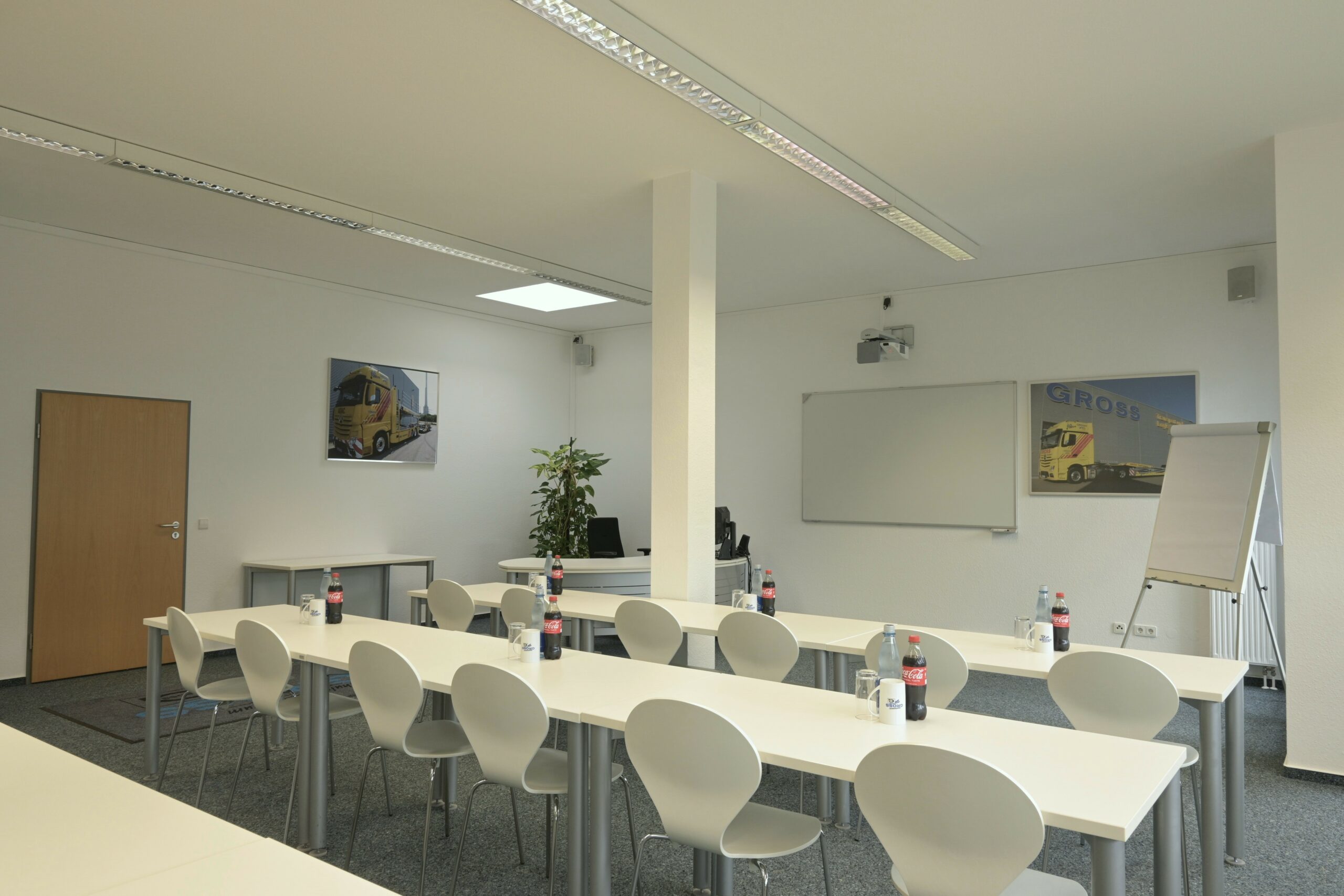 Heller Seminarraum mit weißen Tischen, Stühlen, Flipchart, Projektor, Getränken und Lkw-Poster an der Wand.
