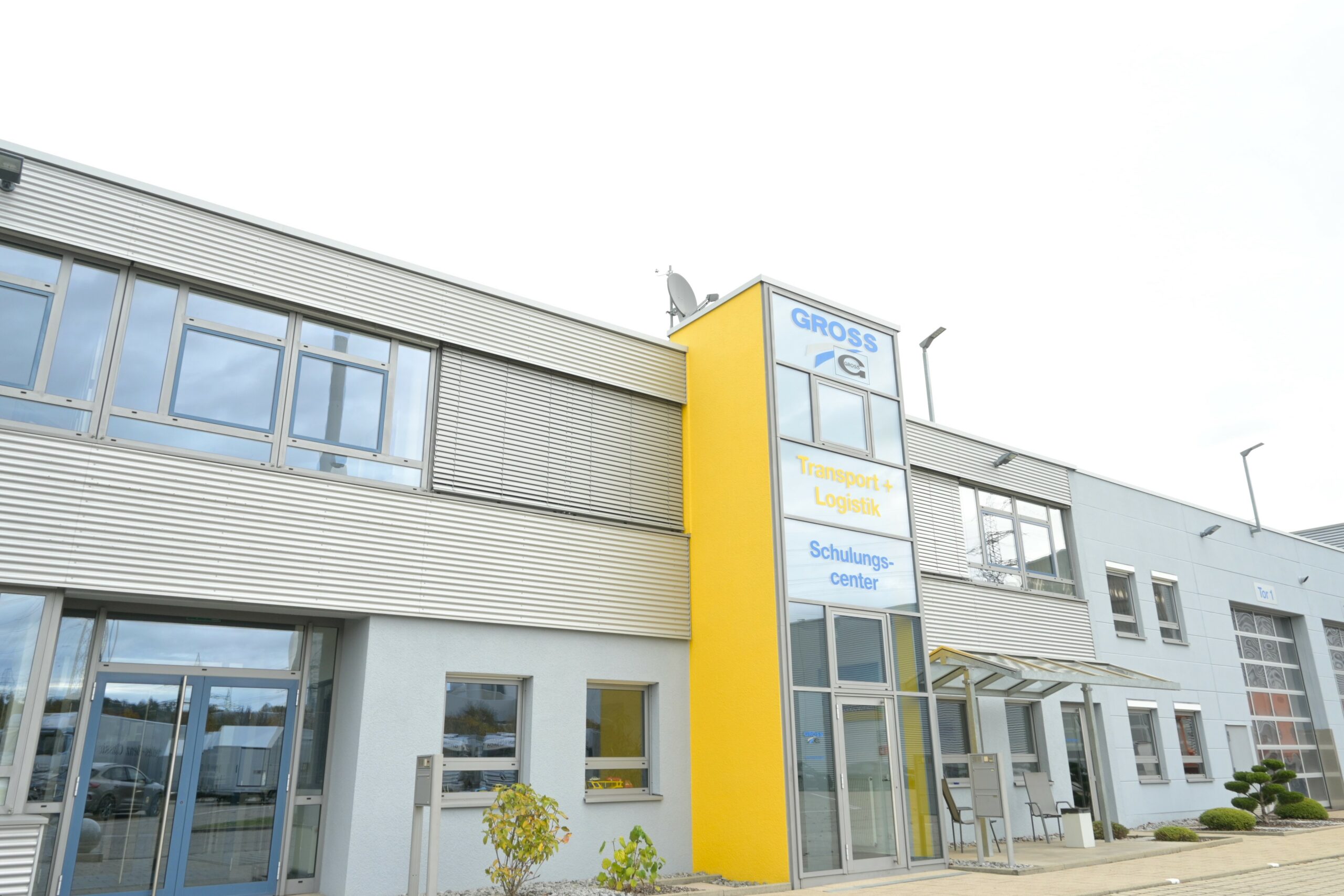 Modernes, zweistöckiges Bürogebäude mit gelbem Eingang, Beschilderung für Transport, Logistik und Schulungscenter.