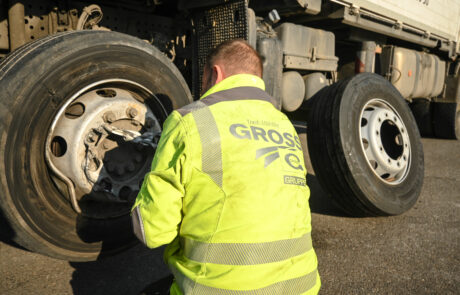 Mann in gelber Jacke überprüft und repariert LKW-Reifen auf offener Straße bei Tageslicht.