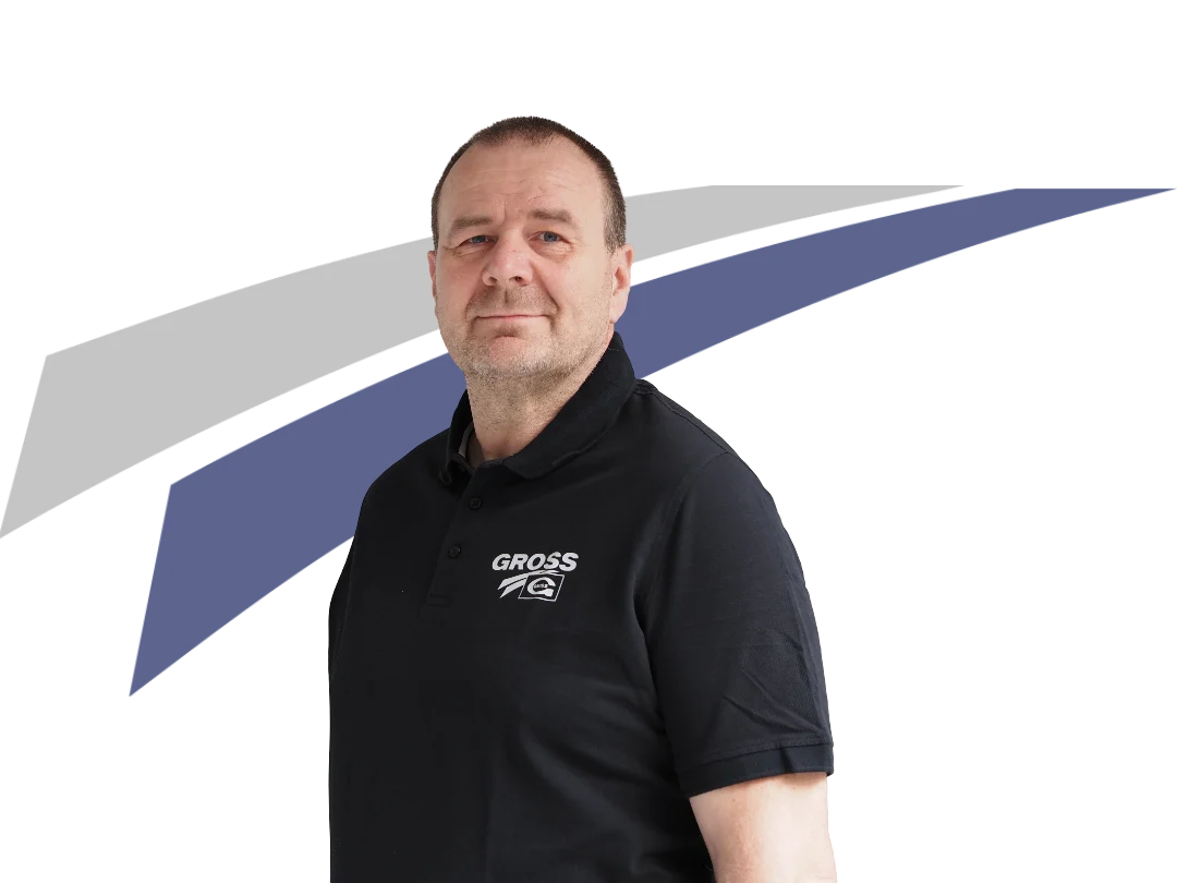 Mann in schwarzem Polohemd mit Logo, vor abstraktem Hintergrund in Weiß, Grau und Blau, schaut neutral in die Kamera.