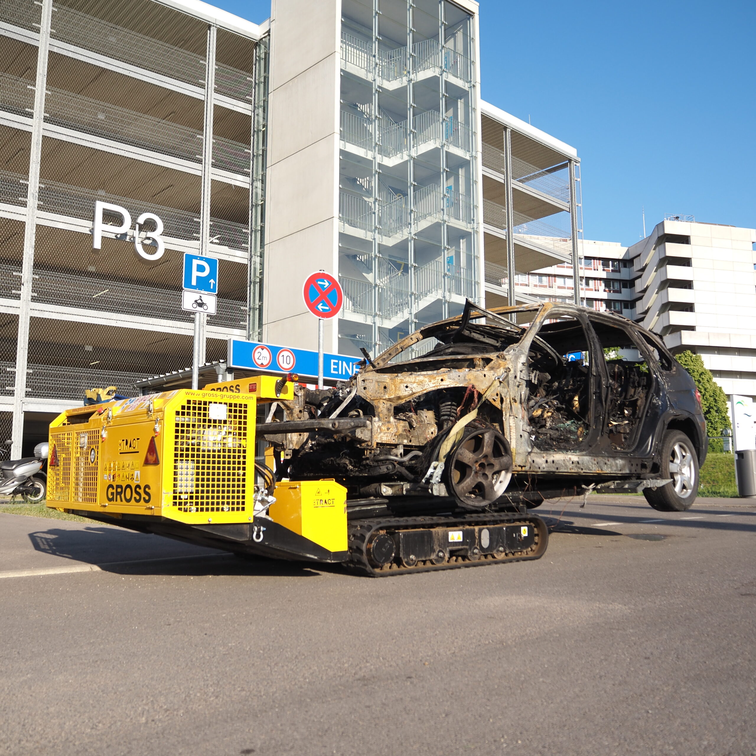 Gelbes Bergungsfahrzeug transportiert ausgeschlachtetes Auto vor Parkhaus P3.