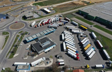 Luftaufnahme eines Parkplatzes voller geparkter Lastwagen neben einem Kreisverkehr und einem Industriegebäude.