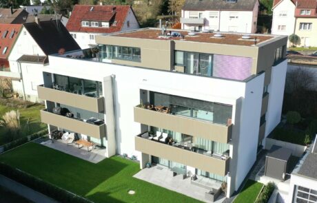 Moderne Wohnanlage mit drei Stockwerken und begrüntem Dach, umgeben von Nachbarhäusern, mit Balkonen und gepflegtem Garten.