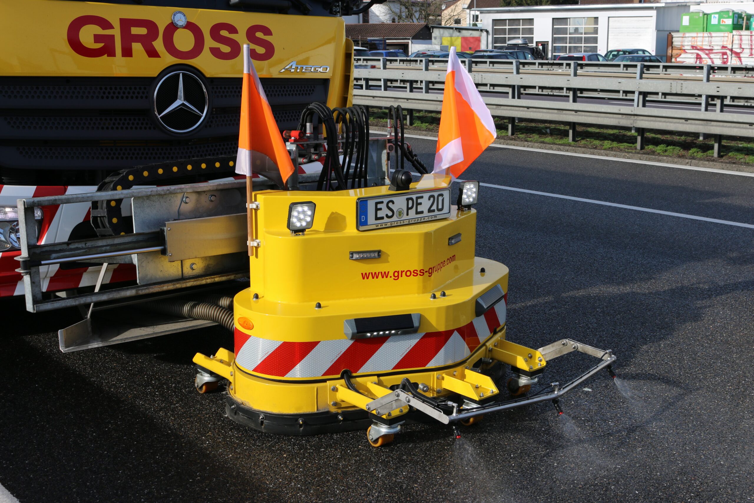 Gelber Straßenwartungs-LKW mit Absicherungsanlage und rot-weißen Warnstreifen auf einer Autobahn.