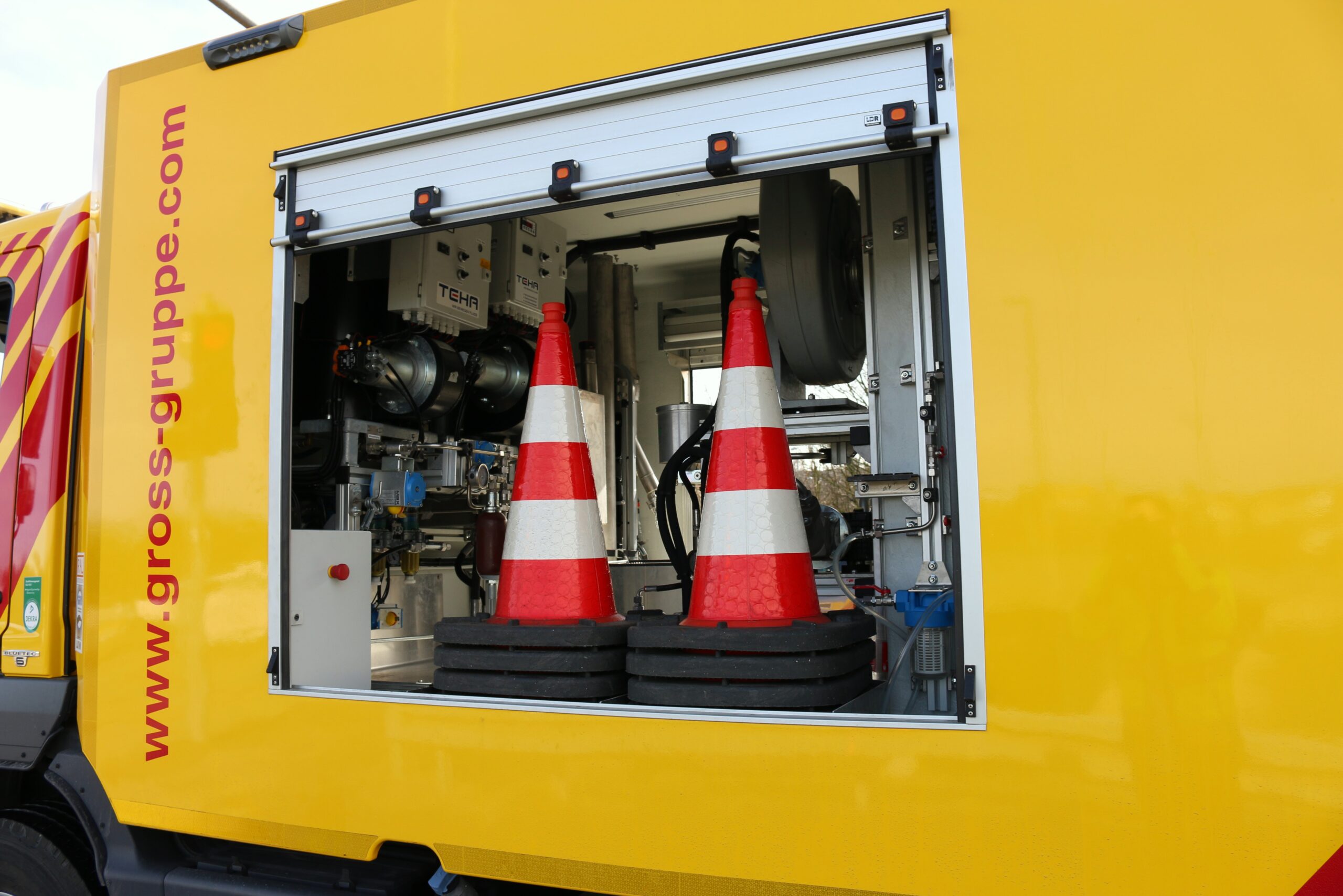 Gelber Lastwagen mit offenem Fach zeigt Ausrüstungen und zwei rot-weiße Verkehrskegel in der Mitte.