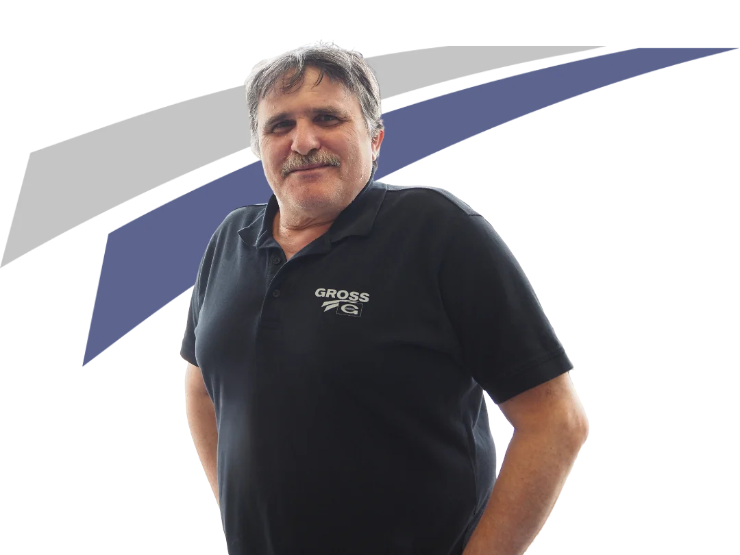 Mann mit kurzem, grauem Haar, schwarzem Poloshirt und lächelndem Gesicht, steht vor einer abstrakten, grafischen Hintergrundgestaltung.