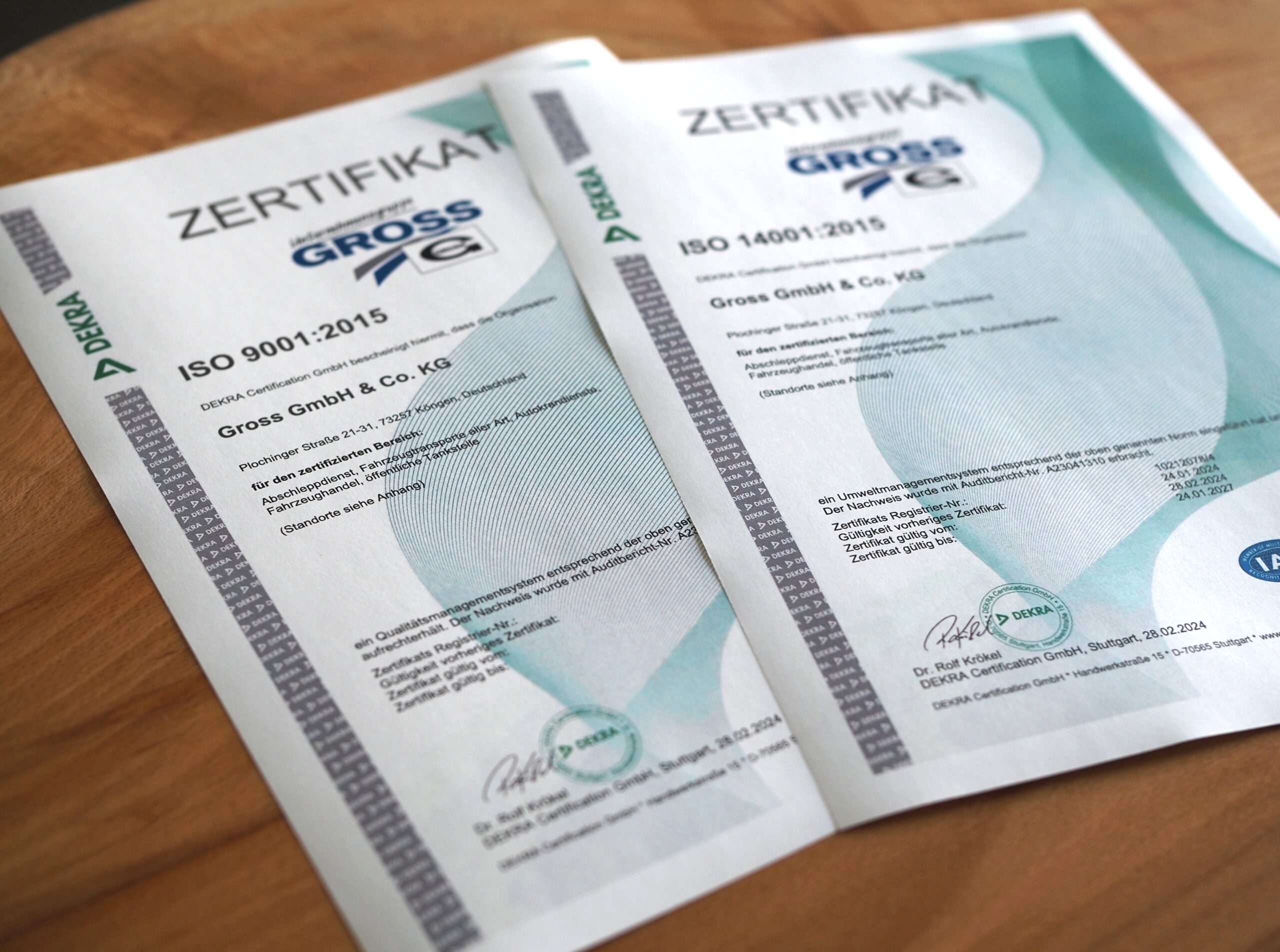 Zwei DEKRA-Zertifikate: ISO 9001:2015 und ISO 14001:2015, ausgestellt für Gross GmbH & Co. KG auf einem Holztisch.