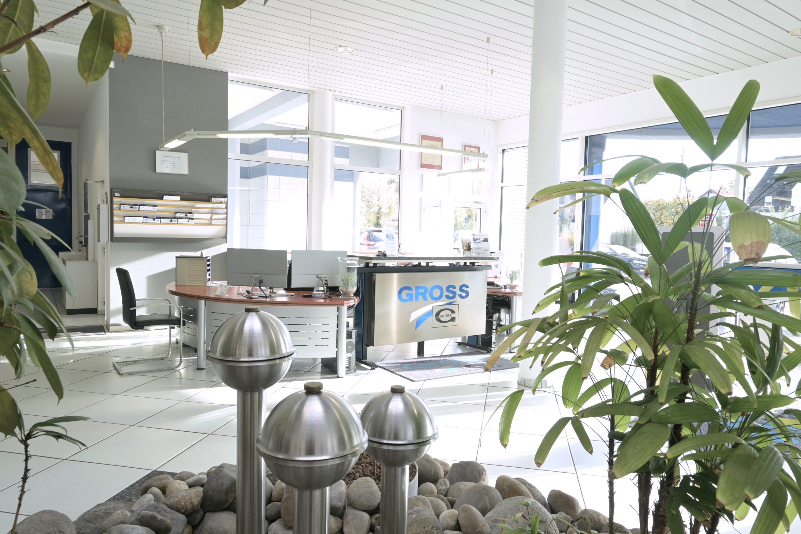 Modernes Büro mit Glaswänden, Pflanzen und Empfangstresen mit Computerbildschirmen, umgeben von Steinen und Edelstahl-Dekoration.