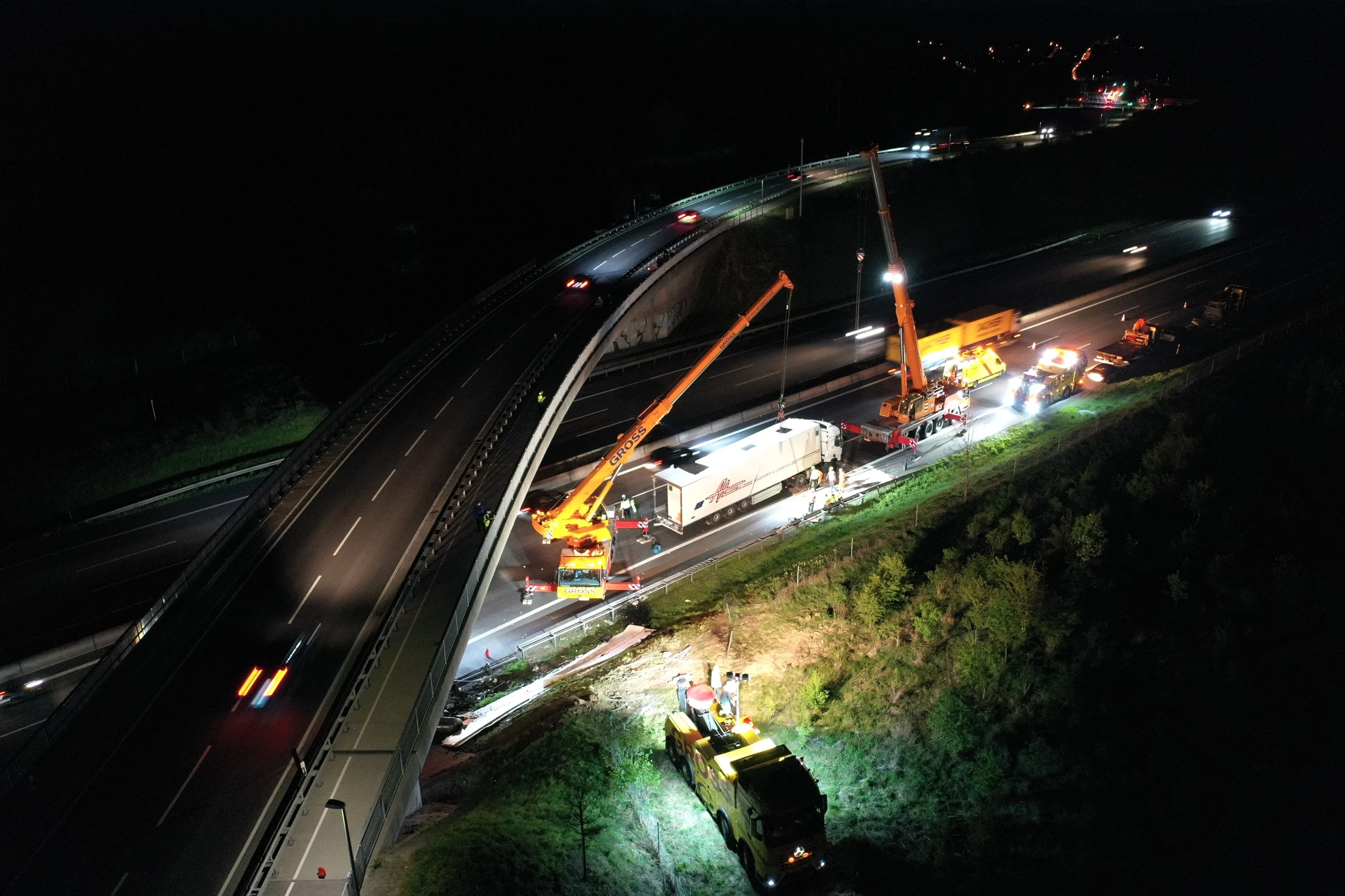 Bauarbeiten bei Nacht auf einer Autobahn: Kran- und Transportfahrzeuge sichern eine Unfallstelle.