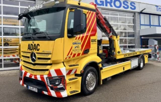Gelber ADAC Abschleppwagen mit rotem Kran, vor einer Werkstatt mit GROSS-Beschriftung.