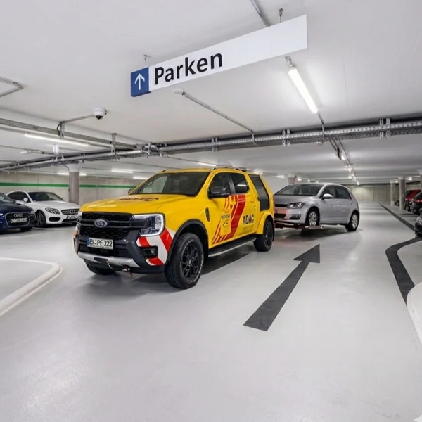 Gelbes ADAC-Fahrzeug parkt in einer Tiefgarage mit Parkhinweisschild und weiteren Autos im Hintergrund.