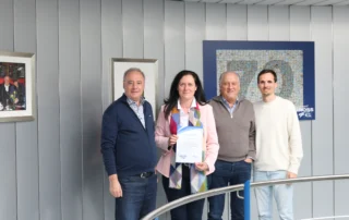 Drei Männer und eine Frau halten eine Urkunde in einem modernen Gebäude, umgeben von Bildern und dekorativen Wänden.