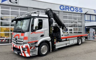 Silberner Lkw mit Kran der Firma Gross vor einem modernen Gewerbegebäude, beschriftet mit „GROSS“.