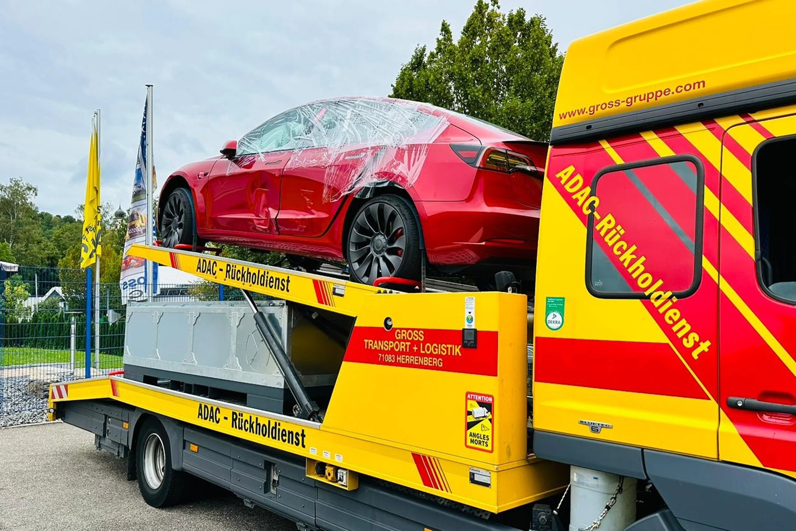 Rotes Auto auf einem ADAC-Rückholdienst-Transporter, mit Folie geschützt, im Freien auf einer Laderampe.