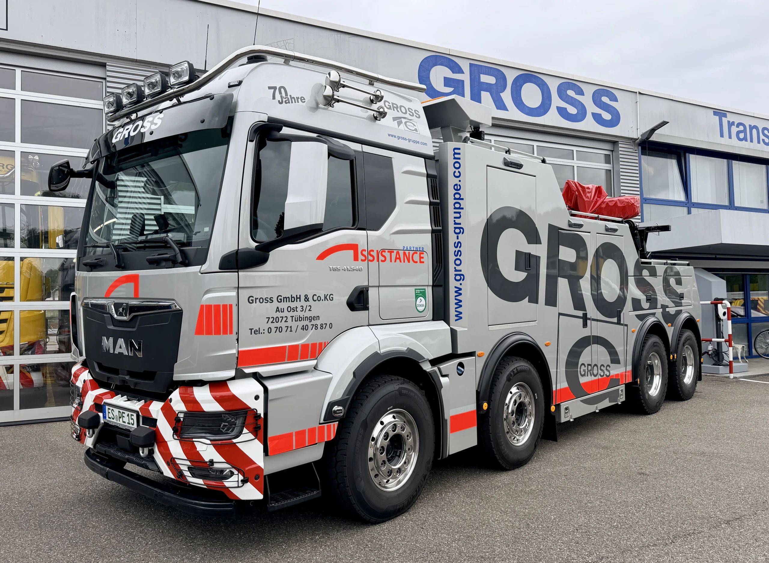 MAN-Lkw mit rotem Abschleppsystem, beschriftet mit GROSS, vor einer modernen Firmengebäude.