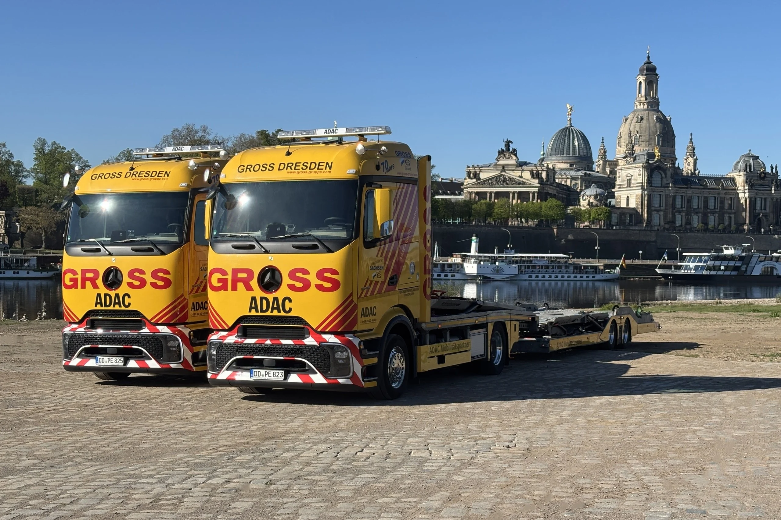 Zwei gelbe ADAC-Lkw stehen am Ufer der Elbe vor der historischen Dresdner Altstadt.