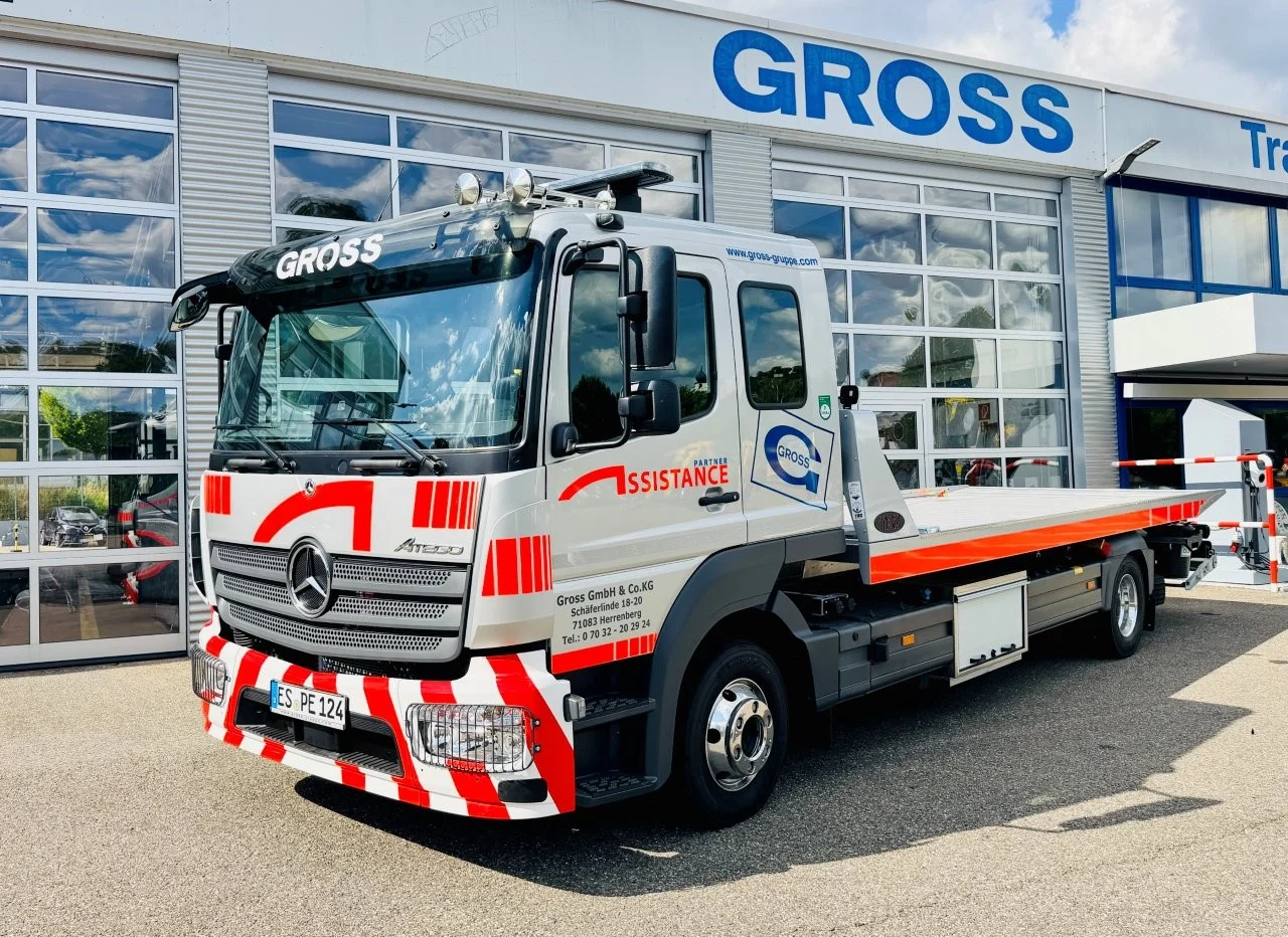 Transporter der Firma GROSS vor einem Gebäude, mit orangefarbener Ladefläche und auffälligen rot-weißen Markierungen.