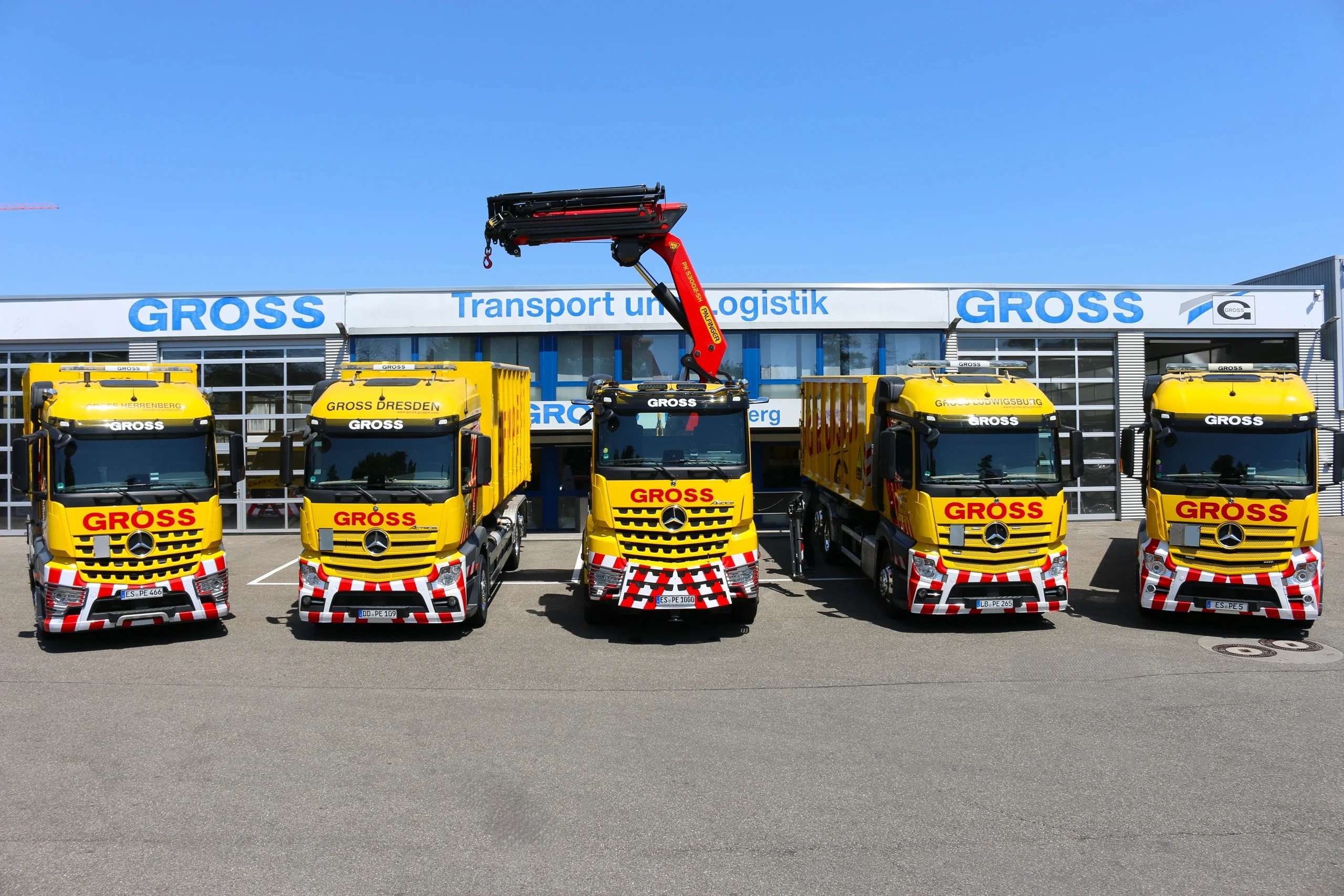 Fünf gelbe Lkw mit der Aufschrift GROSS stehen vor einem modernen Logistikgebäude an einem blauen Himmel.