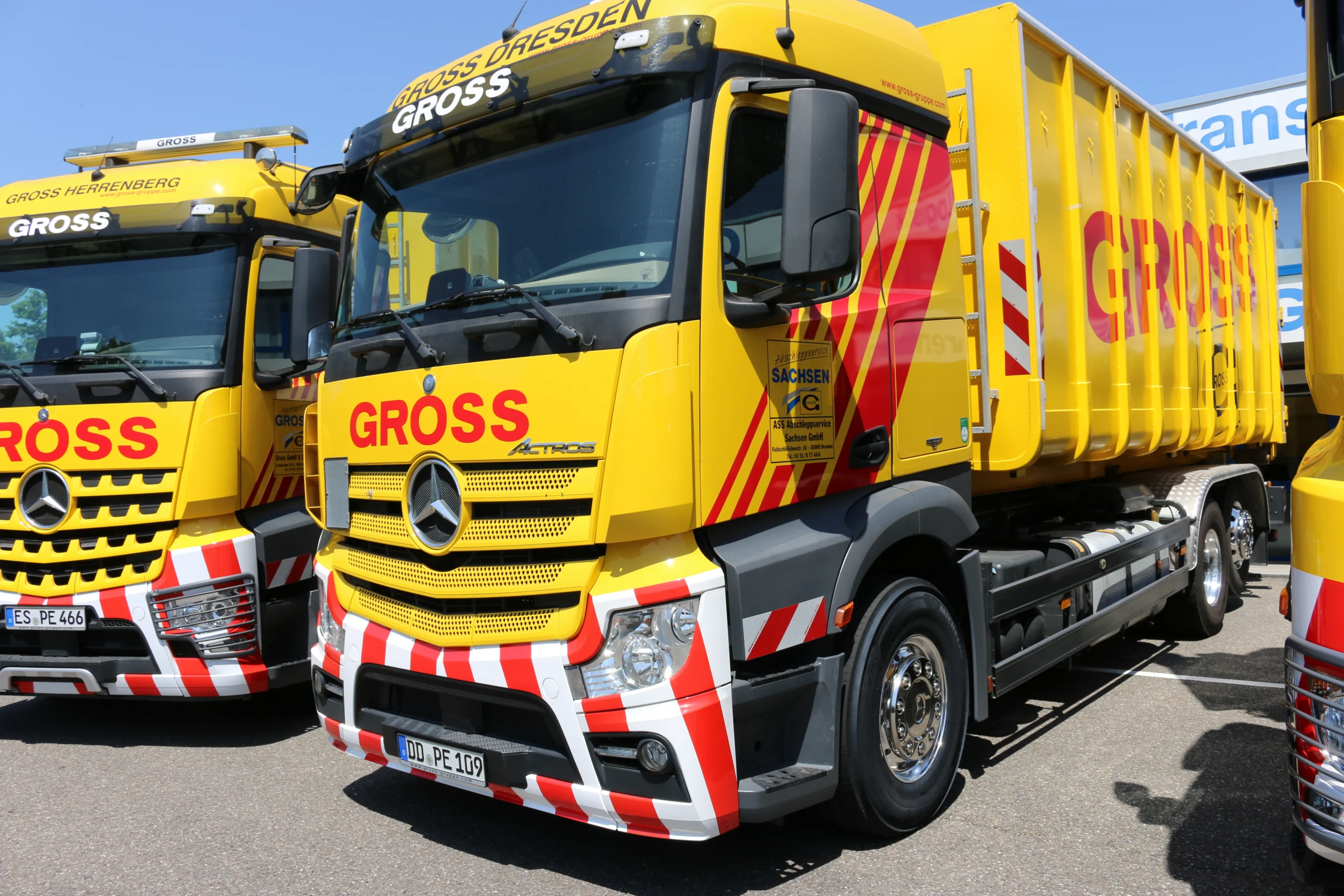 Gelber Lastwagen der Marke Mercedes mit großem Aufdruck GROSS und rot-weißen Streifen. Parkplatzansicht.