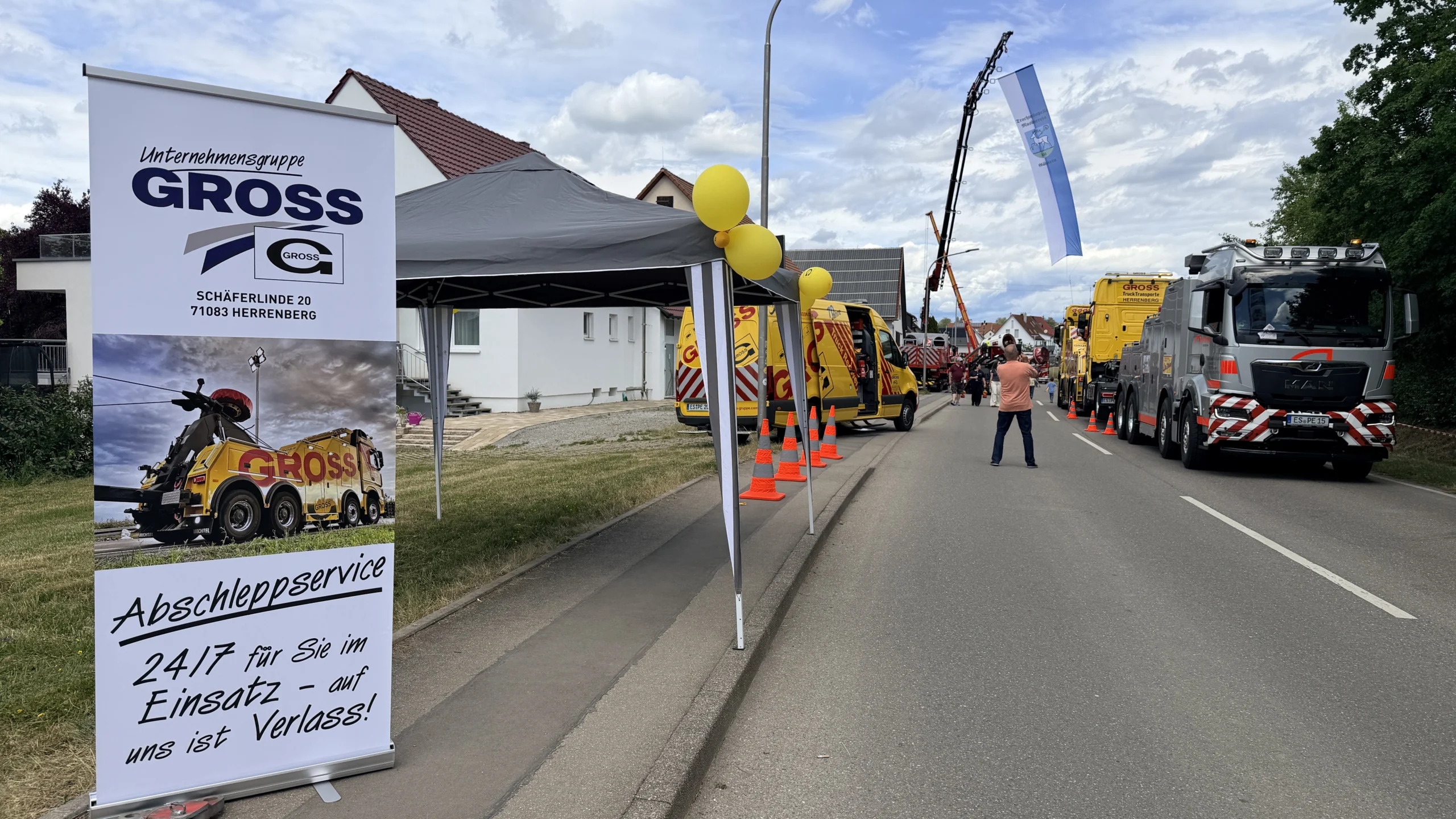 Banner der Unternehmensgruppe GROSS für Abschleppservice, Fahrzeuge und Festdeko mit gelben Luftballons auf der Straße.