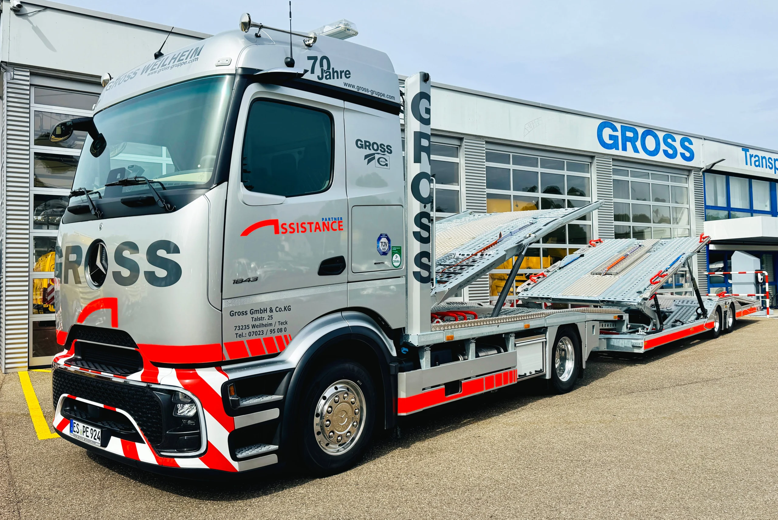 Silberner Lkw mit der Aufschrift GROSS, ausgestattet mit Transportrampen, steht vor einem Unternehmensgebäude.