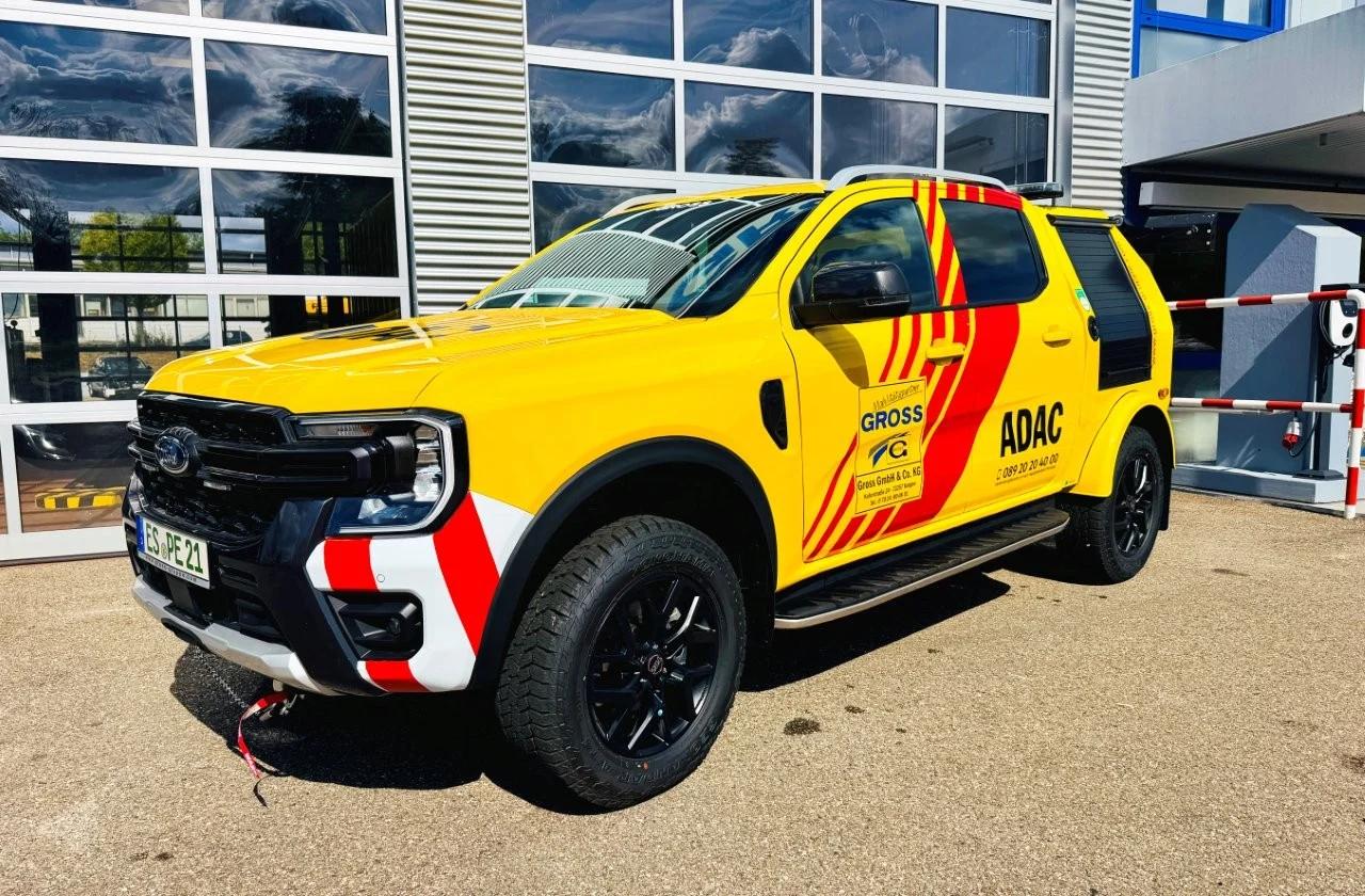 Gelber SUV mit ADAC-Logo und auffälligen roten REFLEKTOREN, steht vor einem modernen Gebäude.
