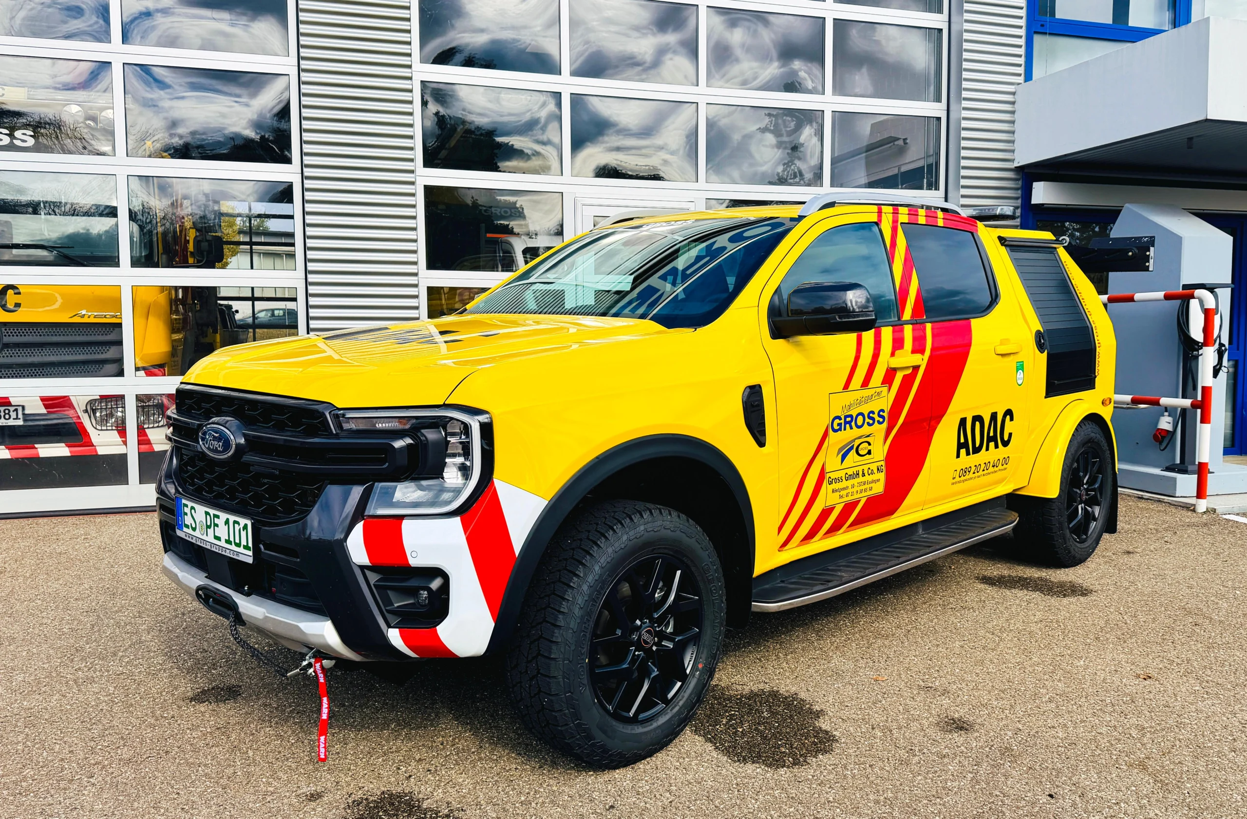 Gelber Ford Geländewagen mit ADAC-Beschriftung steht vor einer Werkstatt, mit schwarzem Grill und reflektierenden Streifen.